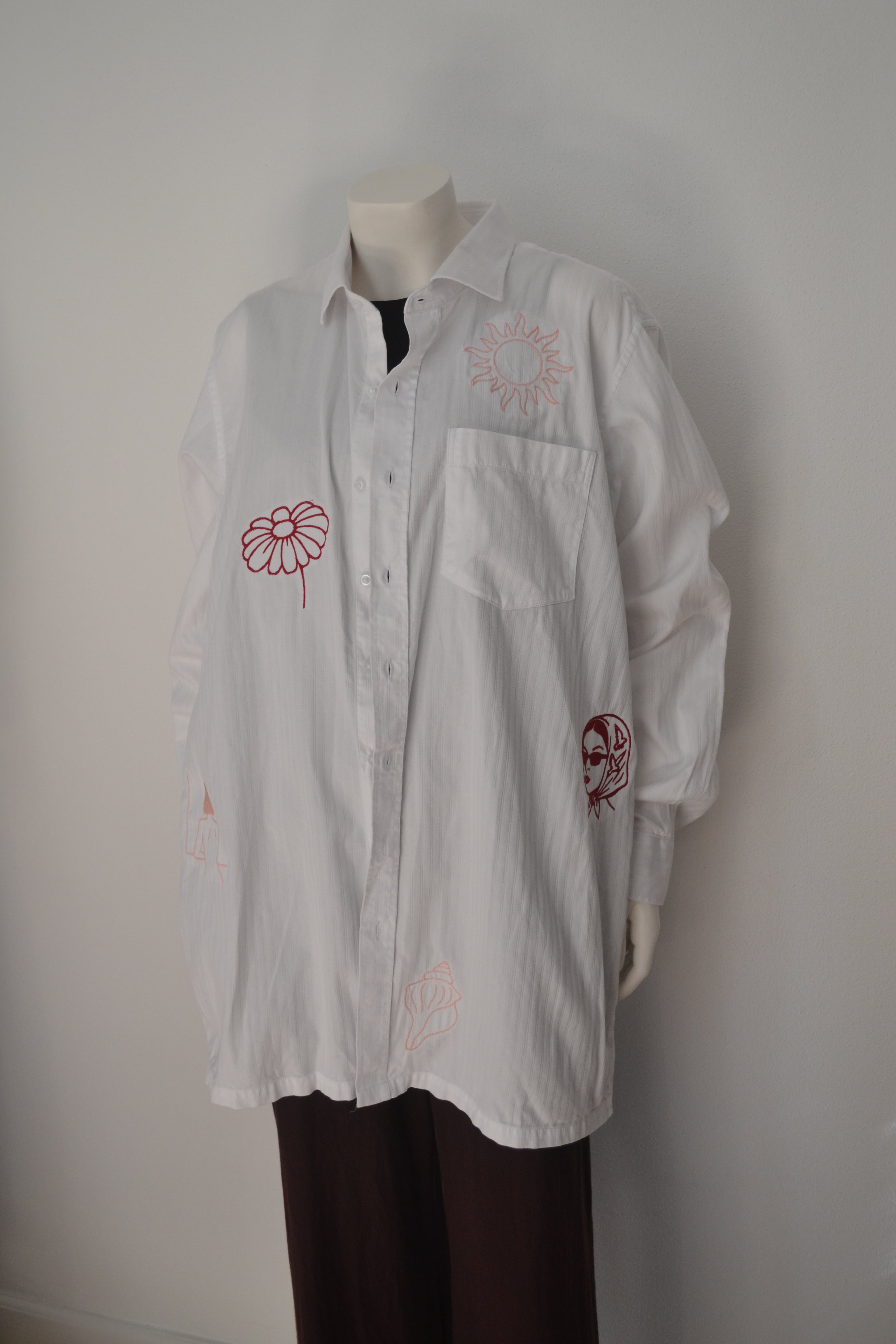 Hvid oversized skjorte forfra med bordeauxrøde broderede motiver — daisy, sol, dame med tørklæde og patches