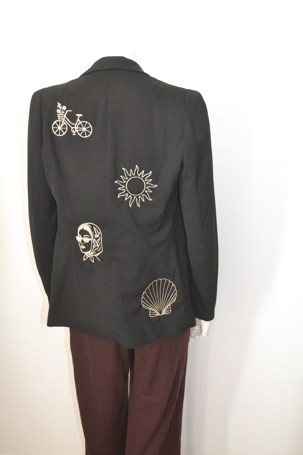 Sort blazer bagfra med cremefarvede broderede motiver — cykel, sol, dame og muslingeskal