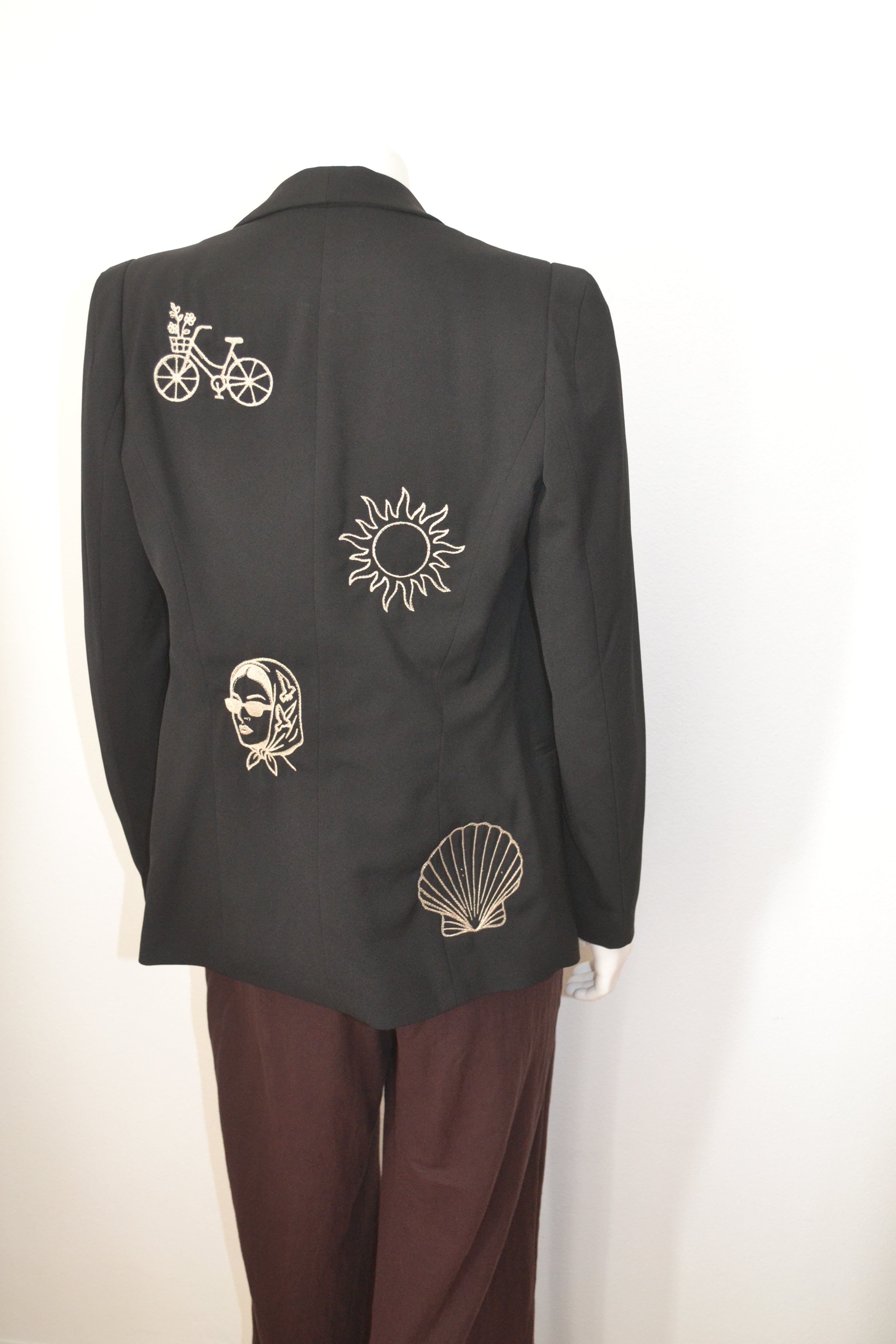 Sort blazer bagfra med cremefarvede broderede motiver — cykel, sol, dame og muslingeskal